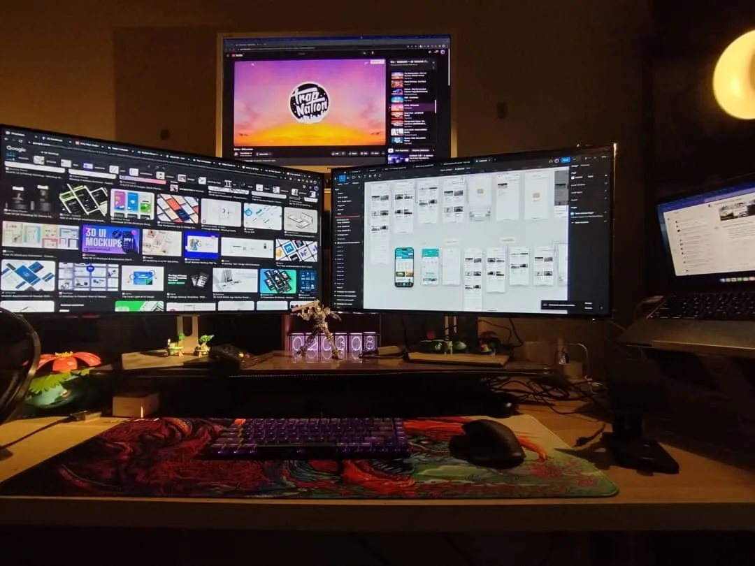 Rasyidun's workstation: three monitors with Figma open, a mechanical keyboard and desk figures